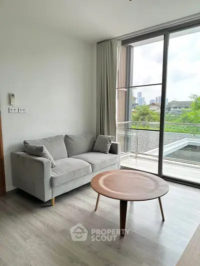 Modern living room with cozy sofa and round wooden table, featuring large windows with city view.