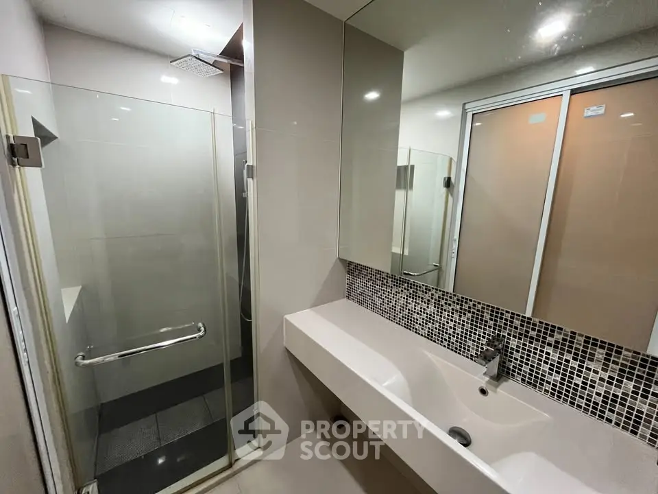 Modern bathroom with glass shower and sleek vanity in contemporary apartment.