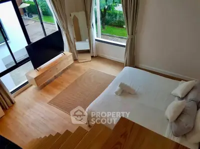 Modern bedroom with large windows, wooden flooring, and stylish decor overlooking a garden view.
