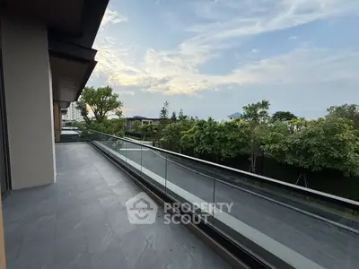 Spacious balcony with glass railing offering serene garden views and modern architecture.