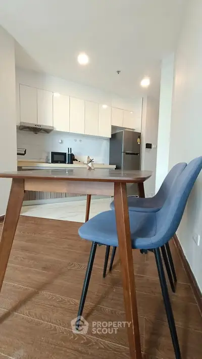 Modern kitchen with sleek cabinets and dining area featuring stylish chairs and wooden table.