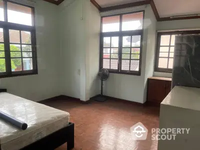 Spacious bedroom with large windows and wooden flooring in a serene residential area.