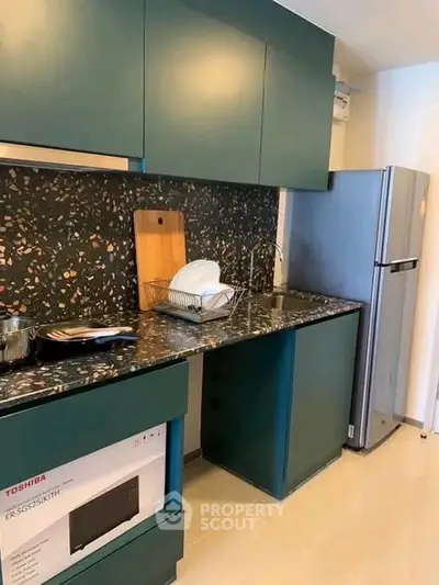 Modern kitchen with sleek cabinets and stylish backsplash, featuring a fridge and microwave.