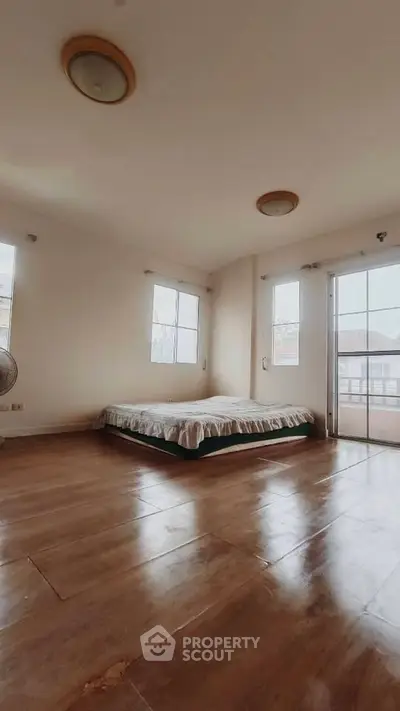 Spacious bedroom with large windows and wooden flooring in a bright, airy apartment.
