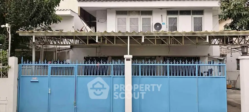 Charming two-story house with blue gate and covered parking area, ideal for family living.