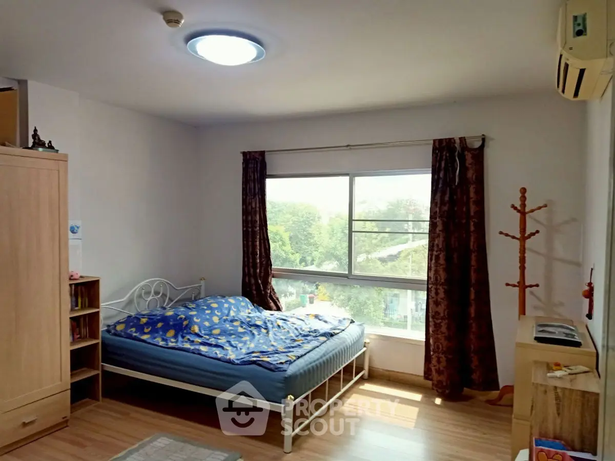 Bright bedroom with large window and wooden flooring, featuring a cozy bed and air conditioning.