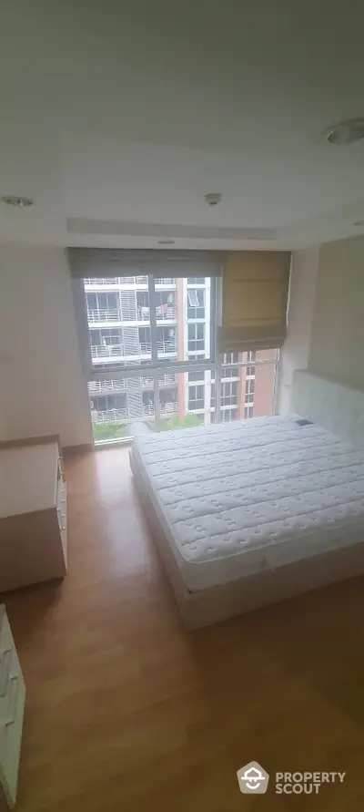 Spacious bedroom with large windows offering ample natural light, hardwood flooring, and a comfortable mattress, perfect for a restful retreat in a modern urban apartment.