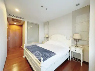 Elegant bedroom with wooden flooring and classic white furniture, featuring a cozy bed and stylish lamps.
