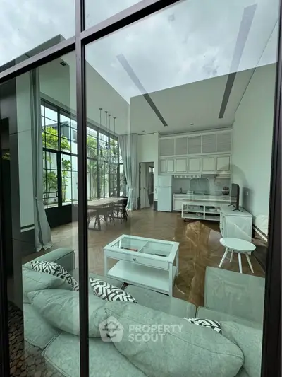 Luxurious modern living room with high ceilings and open kitchen layout, featuring elegant decor and large windows.