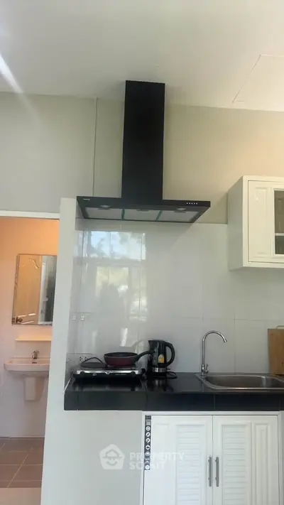 Modern kitchen with sleek black countertop and built-in stove, adjacent to a bathroom with a mirror.