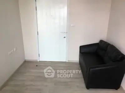 Minimalist room with black leather sofa and white door, perfect for cozy living space.