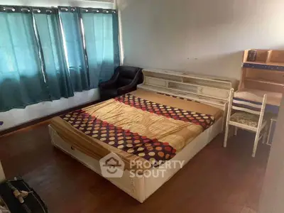 Cozy bedroom with natural light, featuring a bed, chair, and desk for a comfortable living space.