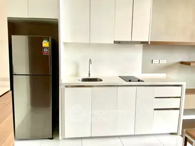 Modern kitchen with sleek white cabinets and stainless steel fridge in a contemporary apartment.