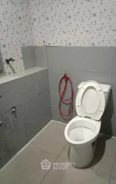 Modern bathroom with tiled walls and floor, featuring a toilet and bidet spray.