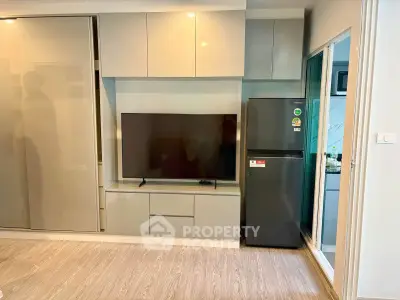 Modern living room with sleek cabinetry and large TV, adjacent to a compact kitchen area.