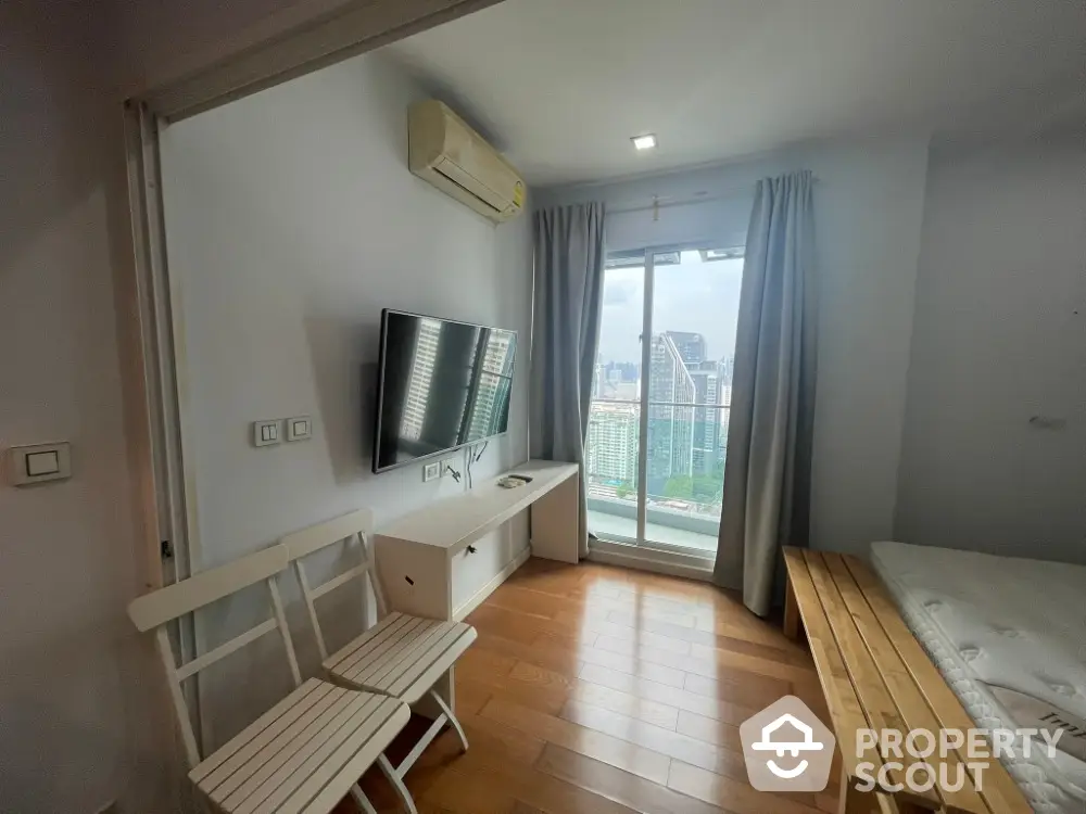 Modern bedroom with city view, wall-mounted TV, and wooden flooring in high-rise apartment.