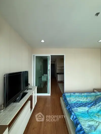 Modern bedroom with wooden flooring and sliding glass doors leading to a hallway, featuring a TV and stylish decor.