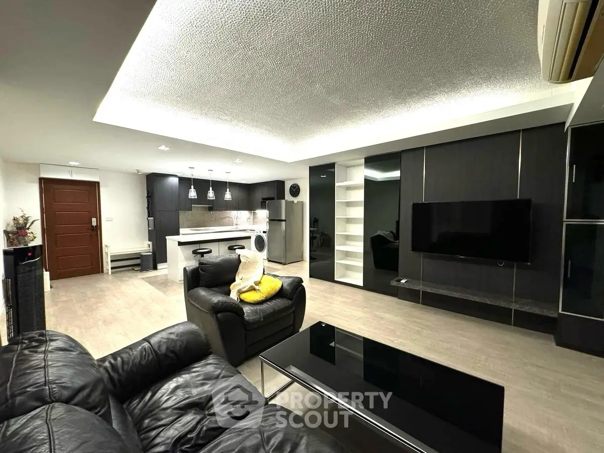 Modern living room with open kitchen, sleek black furniture, and ambient lighting