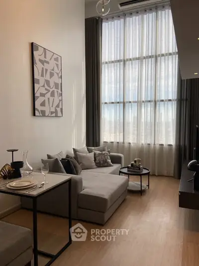 Modern living room with high ceilings and large windows, featuring stylish furniture and elegant decor.