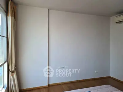 Spacious bedroom with wooden flooring and large window for natural light.