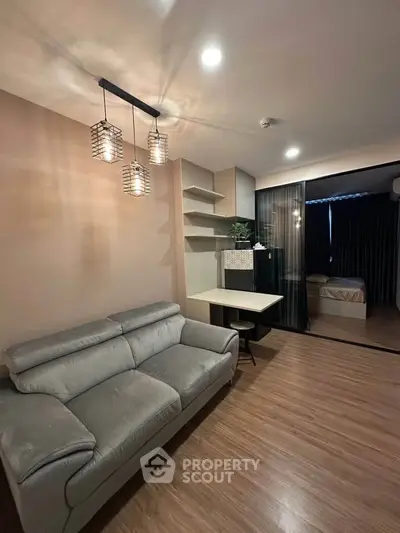 Modern living room with stylish lighting and cozy sofa, featuring a view into a chic bedroom.