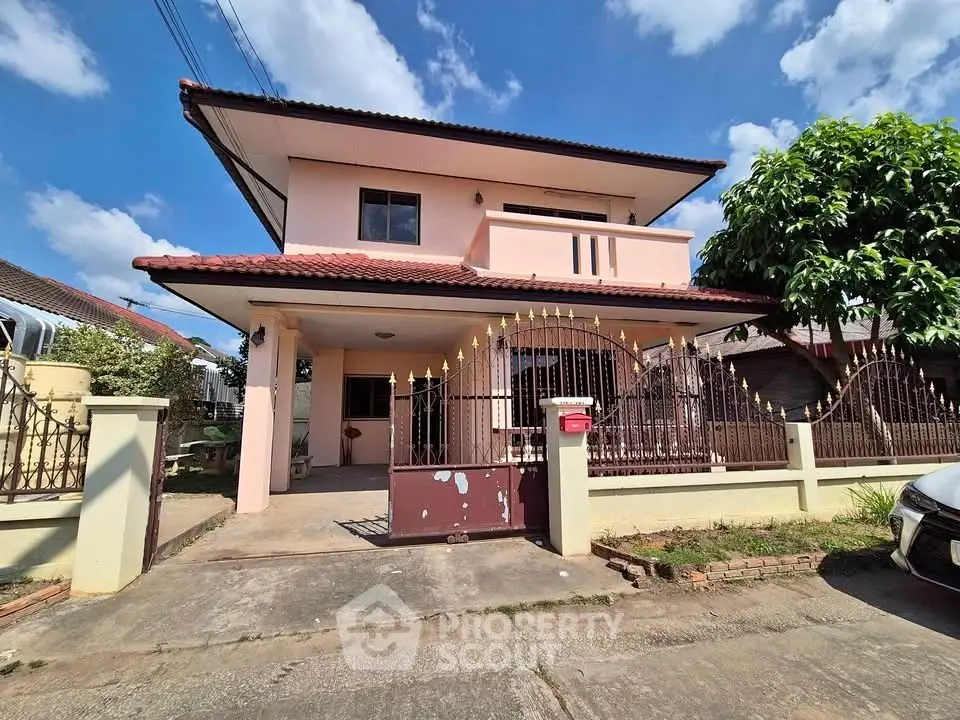 Charming two-story house with gated entrance and lush greenery under a clear blue sky.