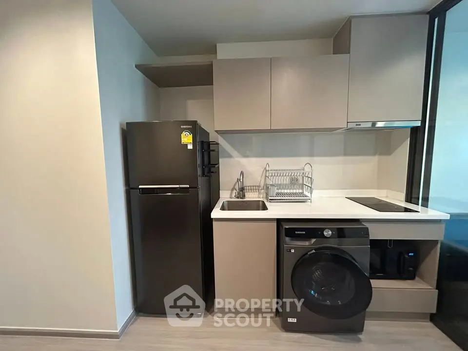Modern kitchen with sleek appliances including fridge, washing machine, and electric stove in compact layout.