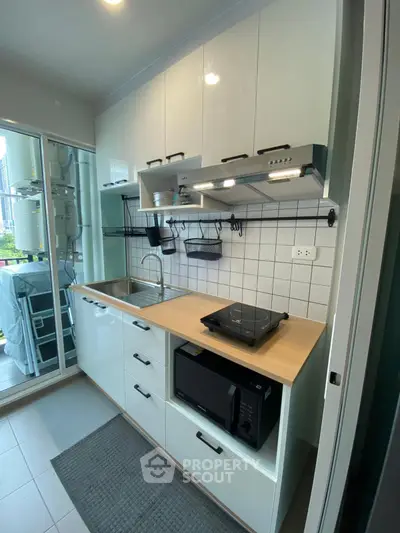 Modern kitchen with sleek cabinetry, induction cooktop, and microwave, featuring a compact and efficient design.