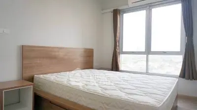 Spacious bedroom with large windows and natural light, featuring a modern wooden bed frame and mattress.