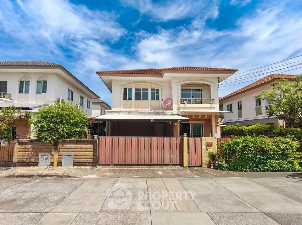 Charming two-story house with gated entrance and lush greenery in a serene neighborhood.