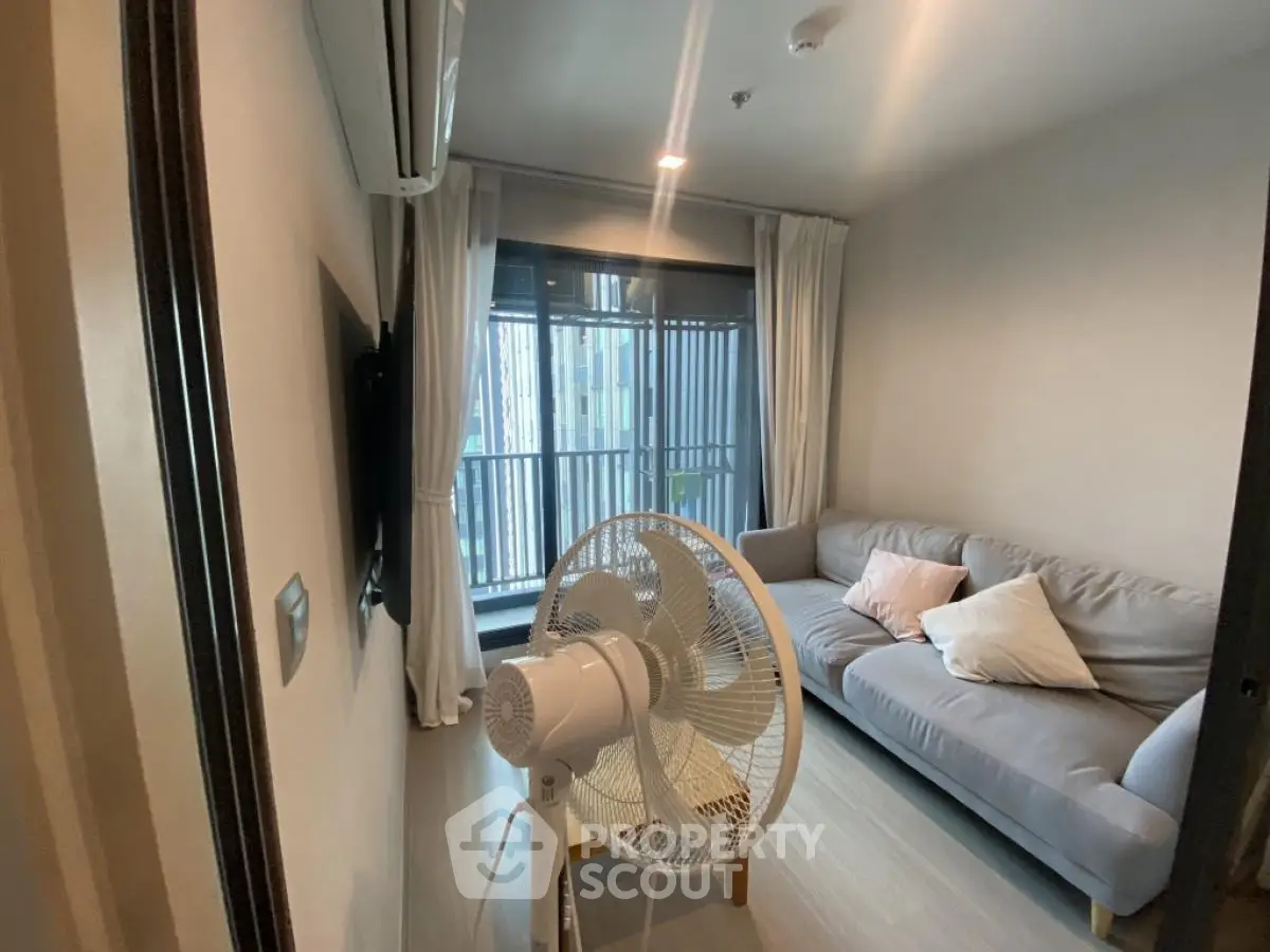 Cozy living room with modern sofa and fan, featuring large windows for natural light.