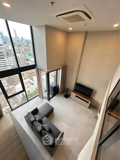 Modern loft-style living room with high ceilings and city view from large windows.