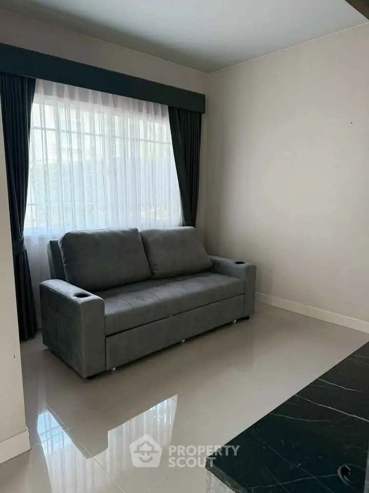 Modern living room with sleek gray sofa and large window with elegant curtains.