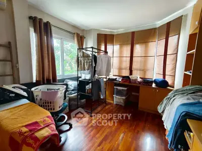 Cozy bedroom with wooden flooring and ample natural light, featuring a large window and practical storage solutions.