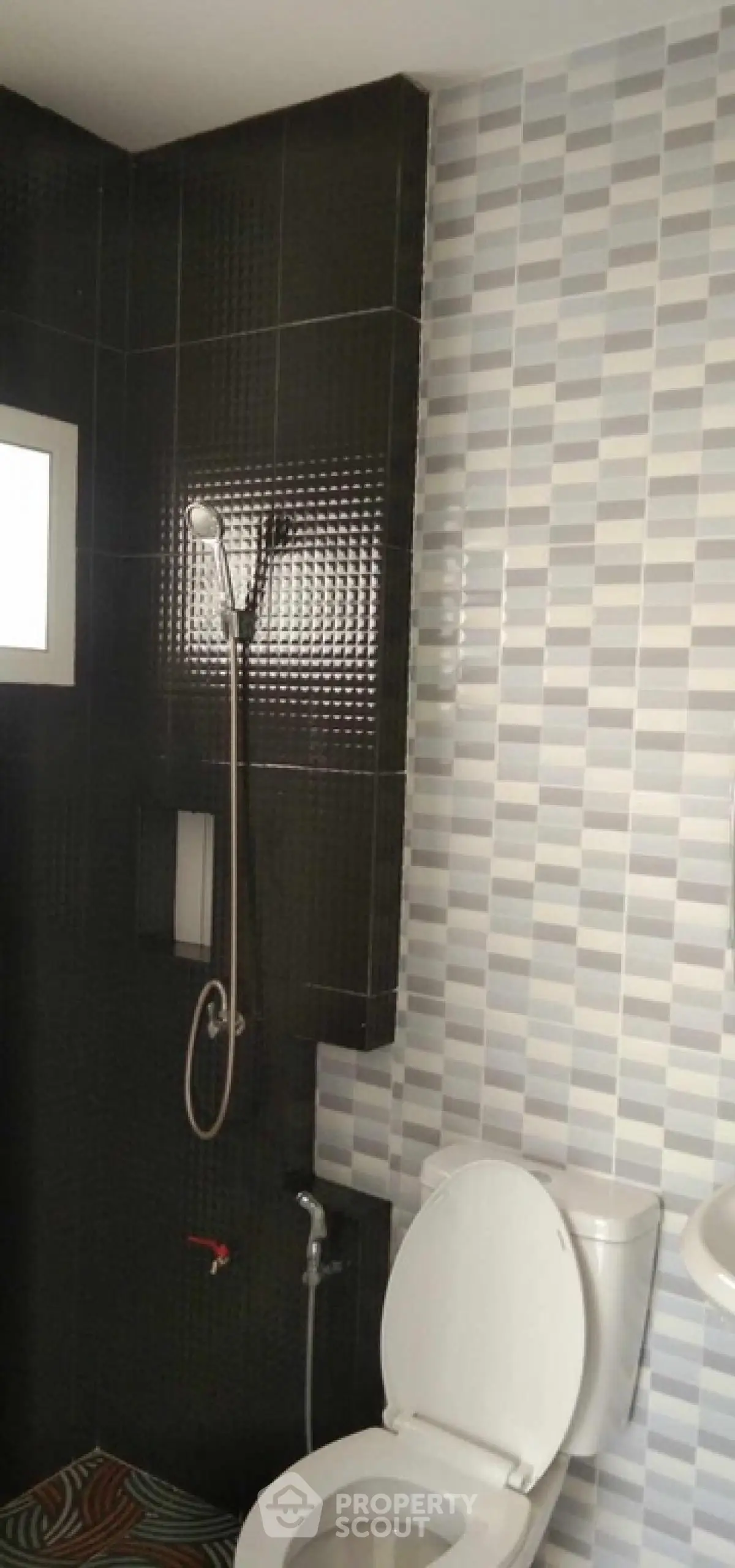 Modern bathroom with stylish black and gray tile design and shower fixture.