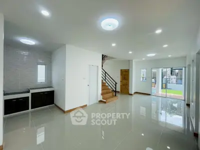 Spacious modern living room with sleek staircase and large windows offering natural light.