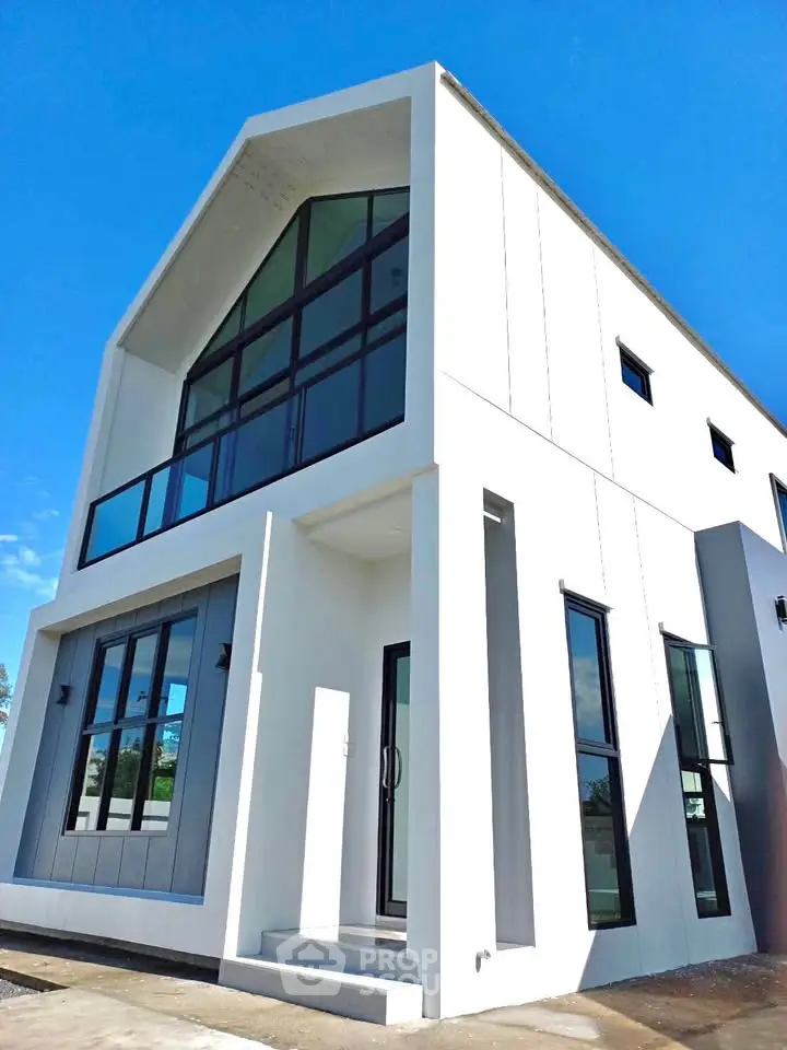 Modern minimalist white house with large windows and sleek design under a clear blue sky.