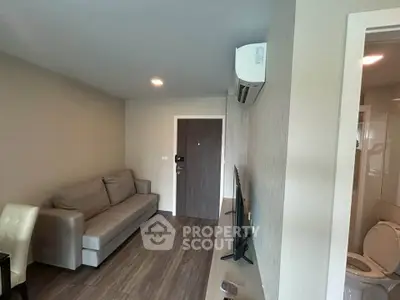 Modern living room with sleek sofa and wall-mounted TV, featuring a glimpse of a bathroom.