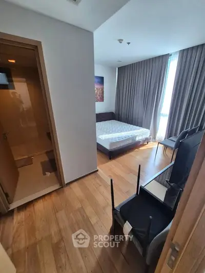 Modern bedroom with wooden flooring, large window, and adjacent bathroom in a stylish apartment.