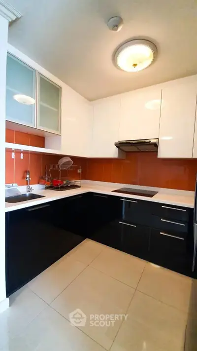 Modern kitchen with sleek black and white cabinetry and orange backsplash