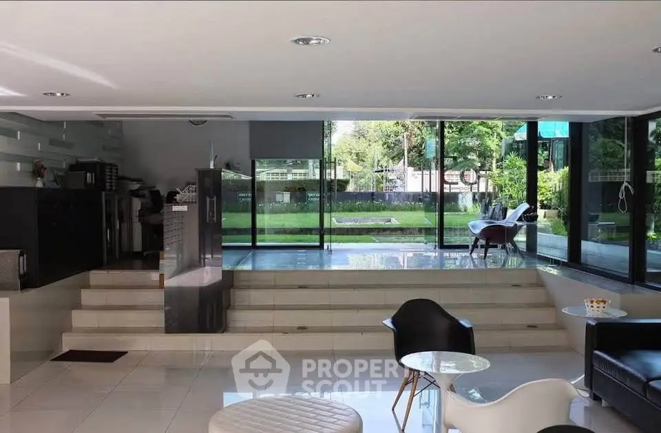 Modern living room with large windows overlooking a lush garden, featuring stylish furniture and sleek design.