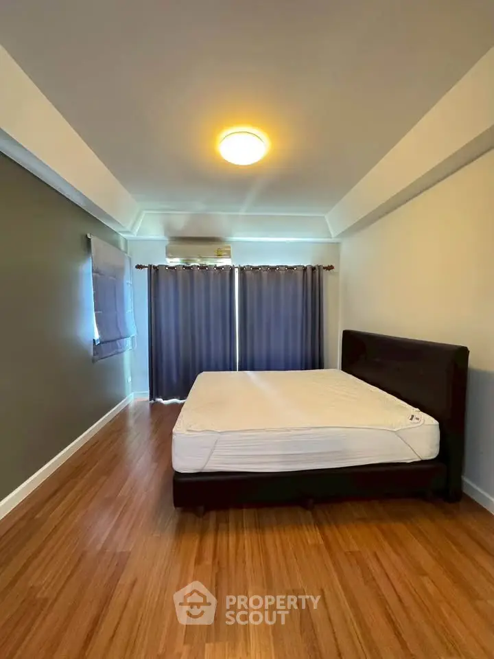 Spacious bedroom with wooden flooring and large window for natural light.