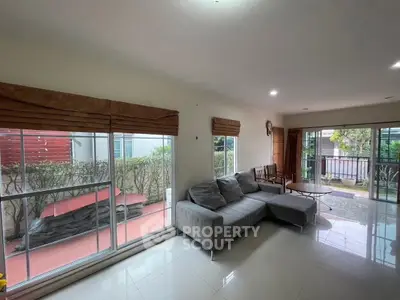 Spacious living room with large windows and garden view, featuring modern gray sofa and natural light.
