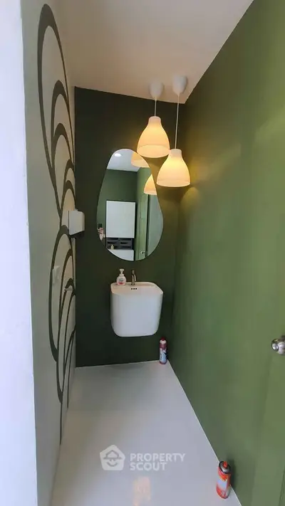 Modern minimalist bathroom with green accent wall and unique mirror design.