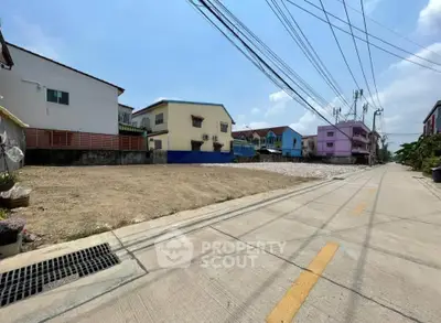 Vacant land plot in a residential neighborhood with clear skies and surrounding houses.
