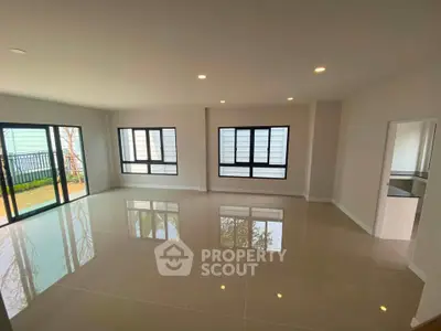 Spacious modern living room with large windows and glossy tiled floors, offering abundant natural light and garden view.