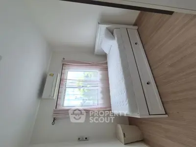 Cozy bedroom with natural light, featuring a white bed and wooden flooring, perfect for relaxation.