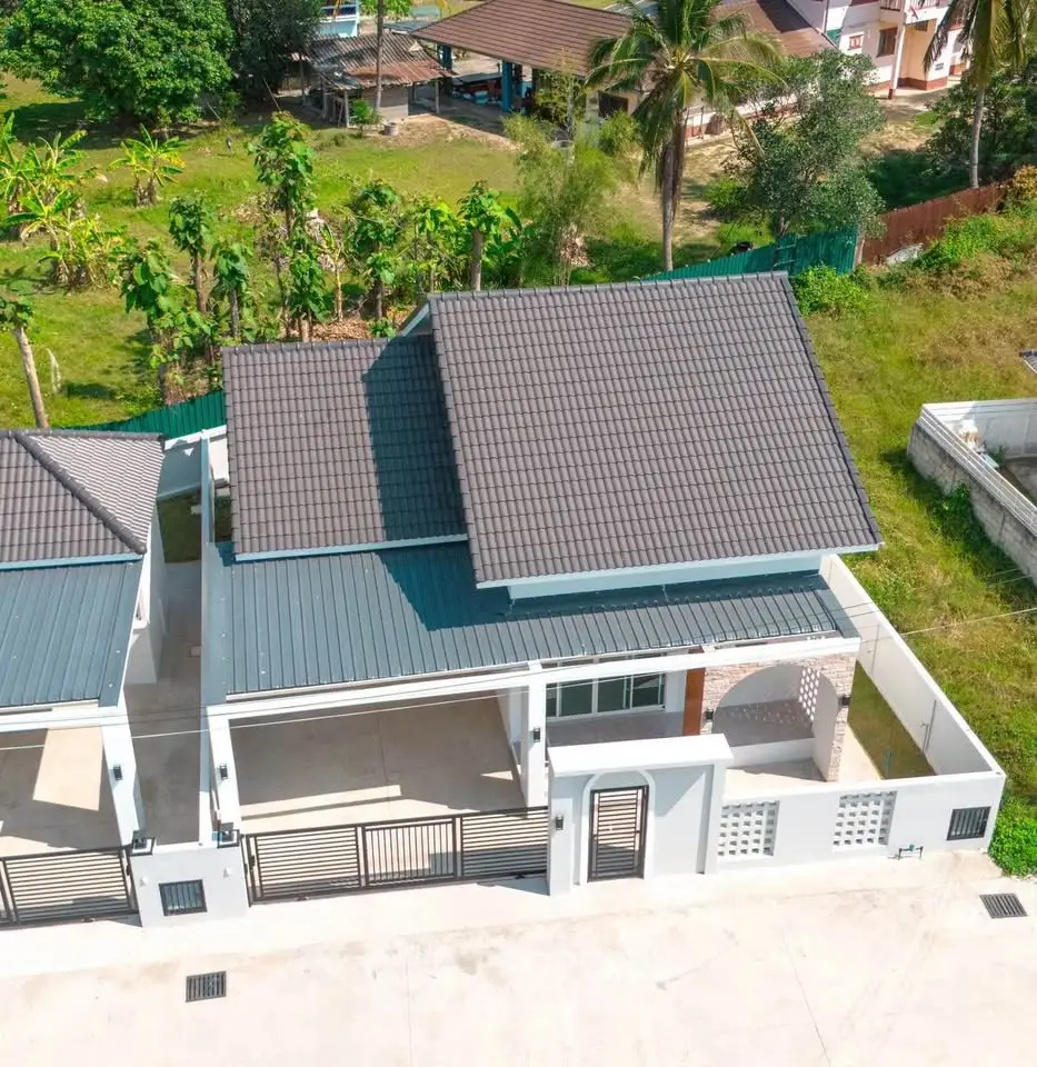 Modern single-story house with sleek roof design and spacious outdoor area in a lush green setting.