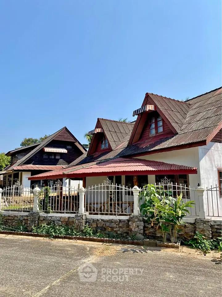 Charming rustic homes with unique roof designs and stone fence under clear blue sky.