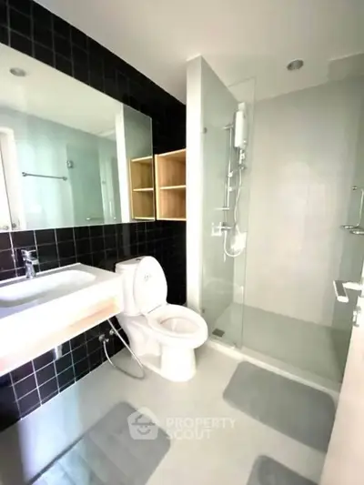 Modern bathroom with sleek design, featuring glass shower and stylish black tile accents.